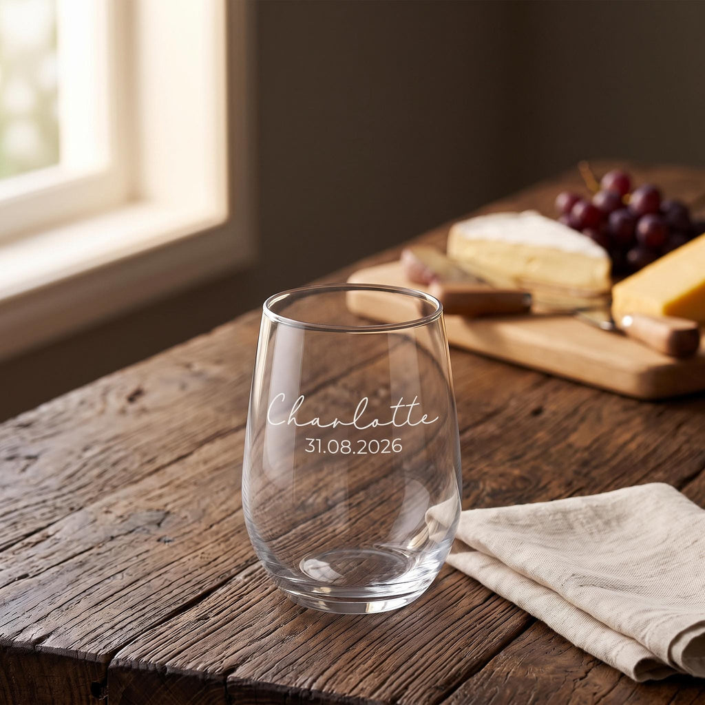 Close up view of a custom etched wine glass resting on a natural timber surface beside a cheese board.