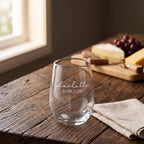 Close up view of a custom etched wine glass resting on a natural timber surface beside a cheese board.