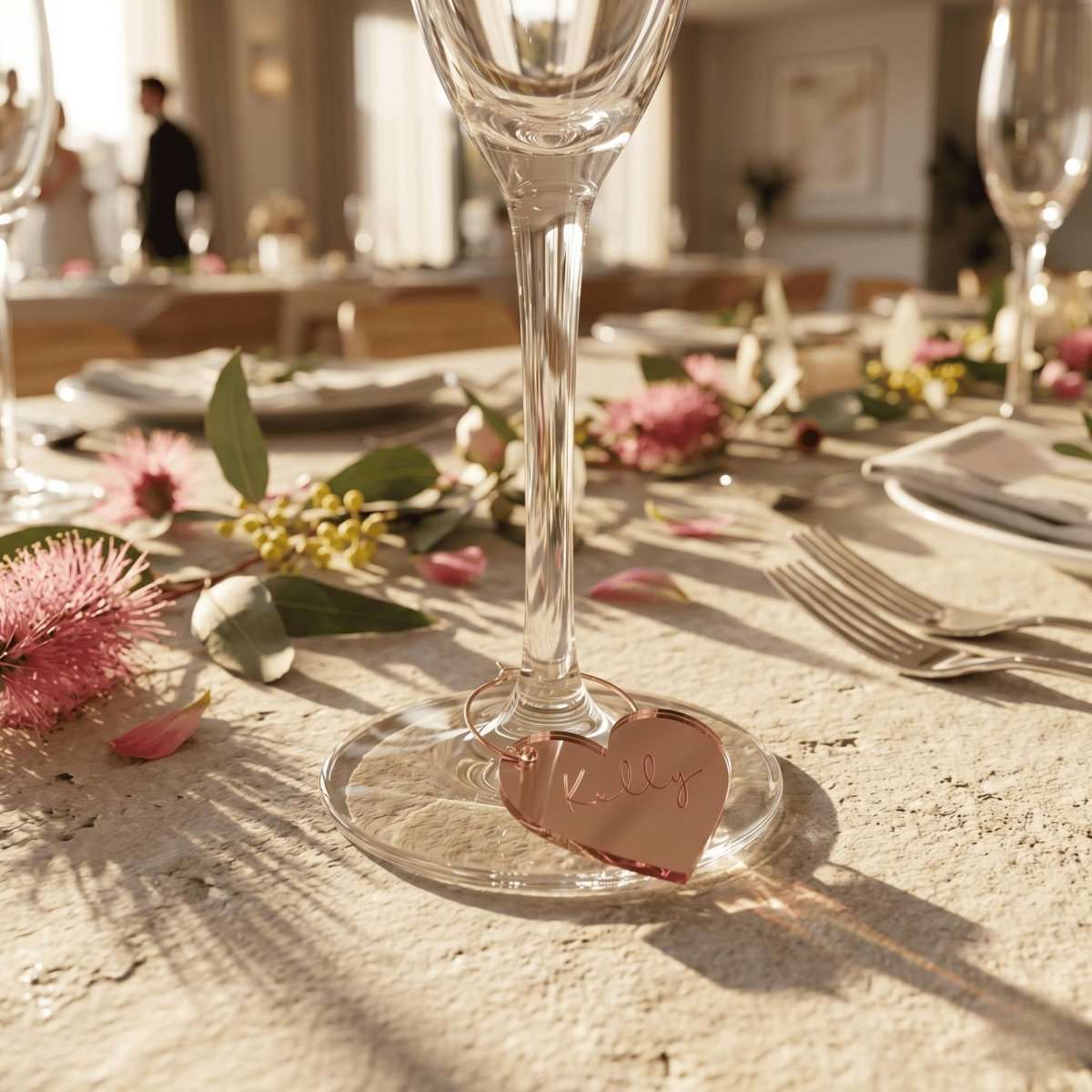 A personalised hooped wine glass charm featuring a custom laser cut guest name in rose gold mirror acrylic clipped onto a gold metal stem hoop, handcrafted by Make It Personal Gift Co in Australia.
