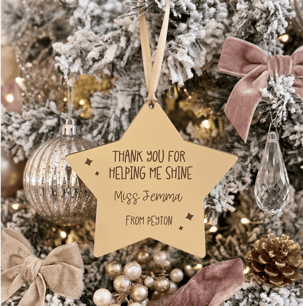 A personalised star-shaped gold mirrored acrylic Christmas ornament hanging on a decorated tree. Engraved text that reads 'THANK YOU FOR HELPING ME SHINE Miss Jemma FROM PEYTON'.