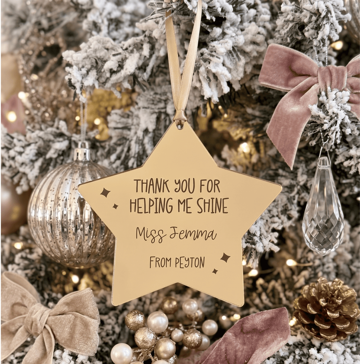 A personalised star-shaped gold mirrored acrylic Christmas ornament hanging on a decorated tree. Engraved text that reads 'THANK YOU FOR HELPING ME SHINE Miss Jemma FROM PEYTON'.