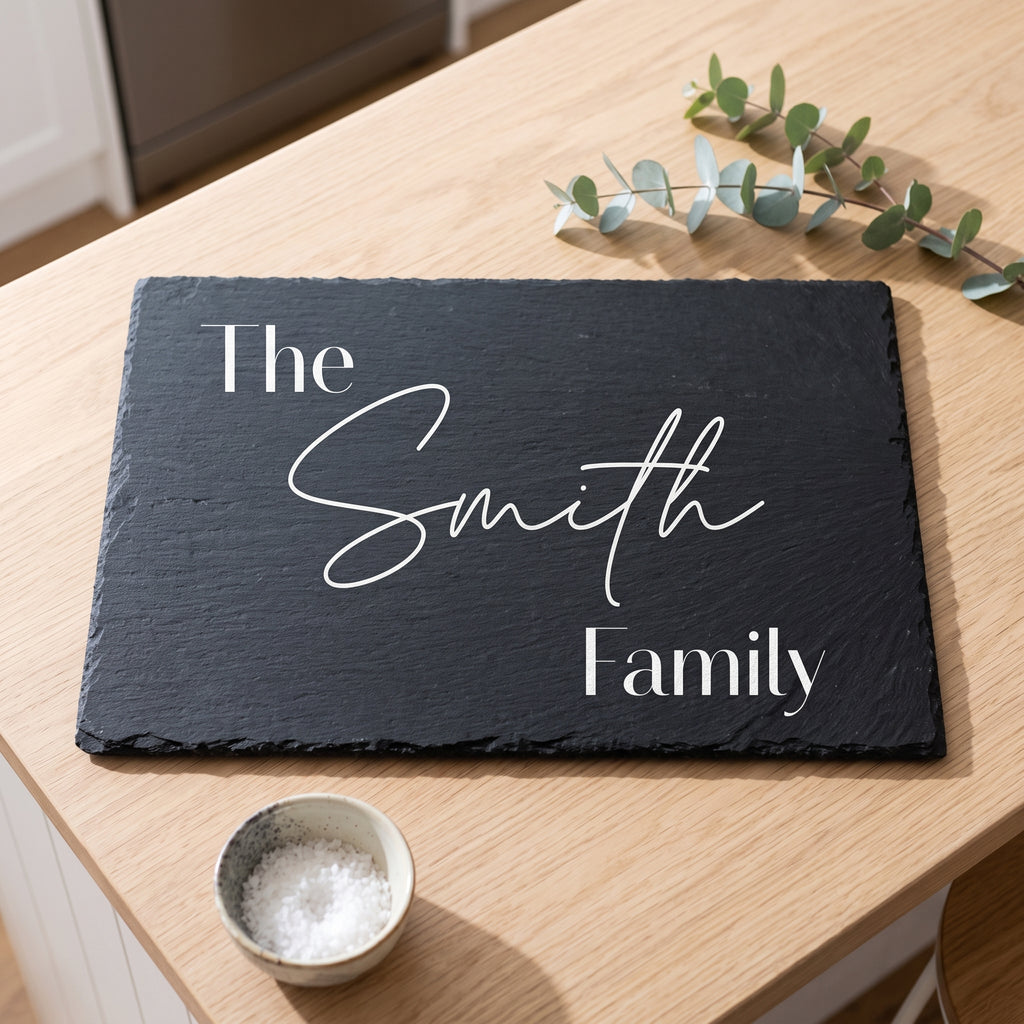 Close up of custom laser engraving on a dark rectangular slate platter showing clean modern lettering and chipped edges.