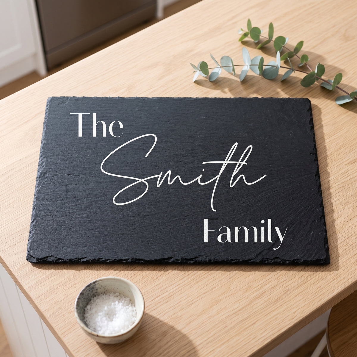 Close up of custom laser engraving on a dark rectangular slate platter showing clean modern lettering and chipped edges.
