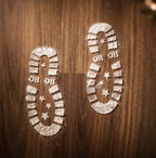 Two boot-shaped footprints made of white powder, including the text 'OH OH' and star details, printed on a dark brown wooden surface.