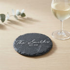 Close up of custom laser engraving on a dark round slate coaster featuring traditional balanced lettering.