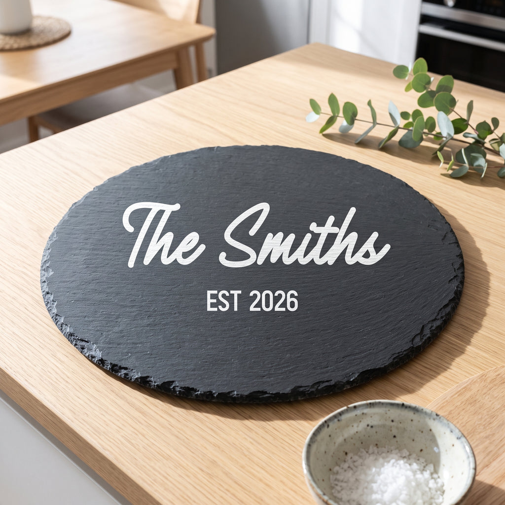 Close up of custom laser engraving on a dark round slate platter showing clear modern lettering and rustic edges.