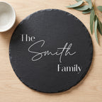 Close up of custom laser engraving on a dark round slate platter showing clean modern lettering and chipped edges.