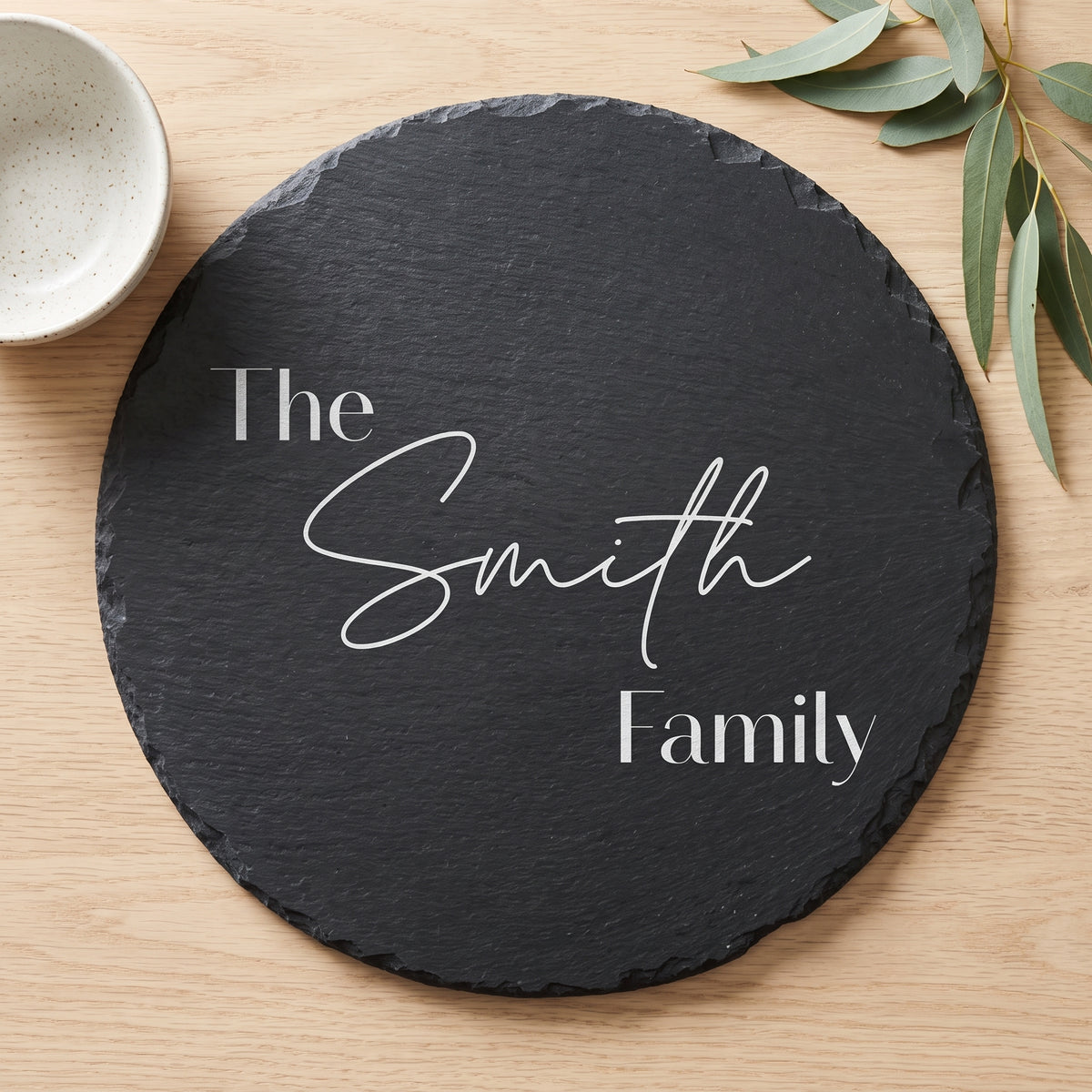 Close up of custom laser engraving on a dark round slate platter showing clean modern lettering and chipped edges.