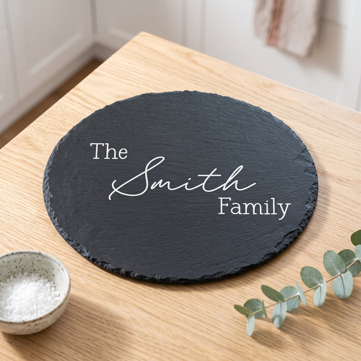 Close up of custom laser engraving on a dark round slate platter showing traditional balanced lettering and chipped edges.
