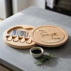 Round wooden cheese board swivelling open to reveal four stainless steel cheese tools stored in interior slots.