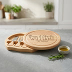 Round wooden cheese board swivelling open to show four stainless steel cheese tools stored in interior slots.
