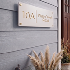 White acrylic house sign with cut out text showing gold backing layer fitted with four gold stand off fixing