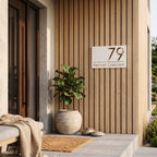 Modern white and gold laser cut house number plaque installed flush on vertical timber entrance wall.